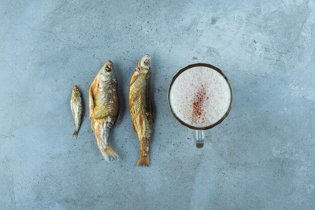 青いテーブルの上にある魚の隣のグラスビール。