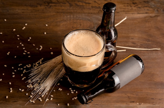 Glass of beer in foam with brown bottles of beer on wooden table