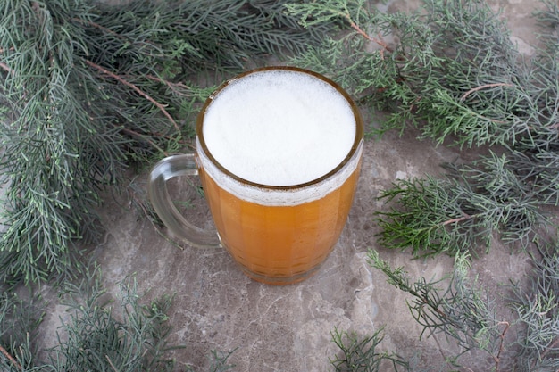 Glass of beer on marble surface with pine branch