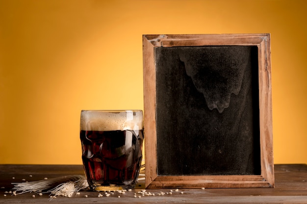 Free photo glass of beer putting next of blackboard on wooden table