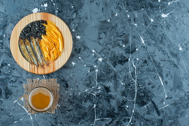A glass of beer on texture and appetizers on wooden plate, on the blue background. 