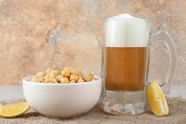 Glass of beer with bowl of peas and lemon slices on table