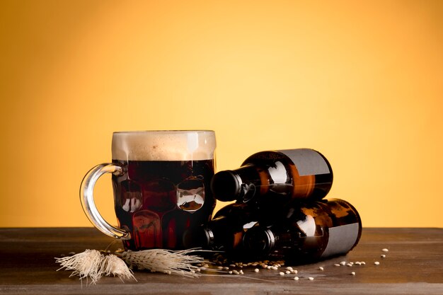 Glass of beer with foam and bottles of beer on wooden table