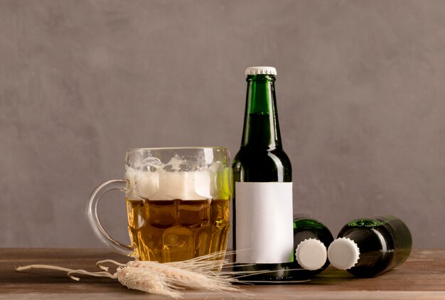 Glass of beer with foam and green bottles of beer on wooden table