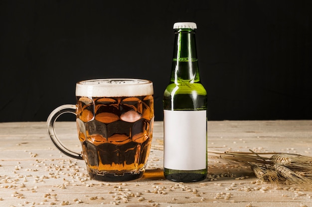 Glass of beer with green bottle and ears of wheat on wooden backdrop