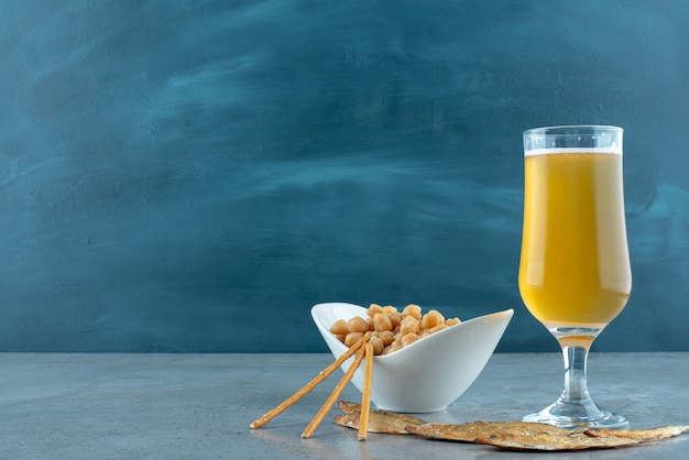 Un bicchiere di birra con piselli e pesce su sfondo grigio. foto di alta qualità Foto Gratuite