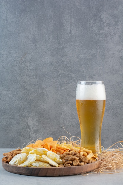 A glass of beer with wheat and potato chips on hay.