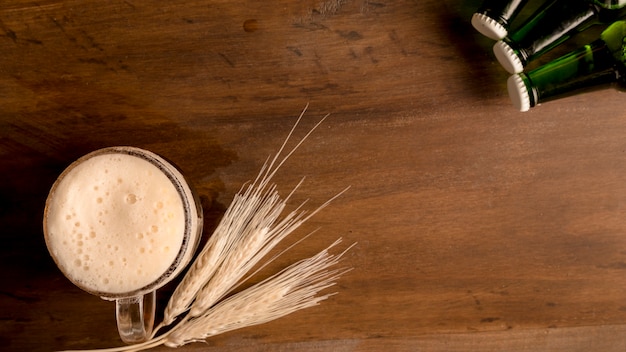 Bicchiere di birra con spiga di grano e bottiglie verdi sul tavolo di legno