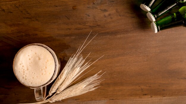 Glass of beer with wheat spike and green bottles on wooden table