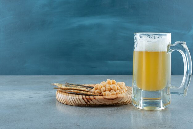 A glass of beer with wooden plate of fish and peas. High quality photo