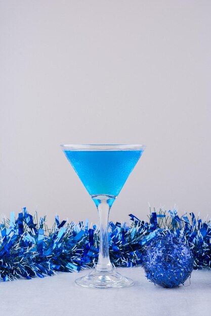 白い表面の青いクリスマスの装飾の横にある青いカクテルのガラス