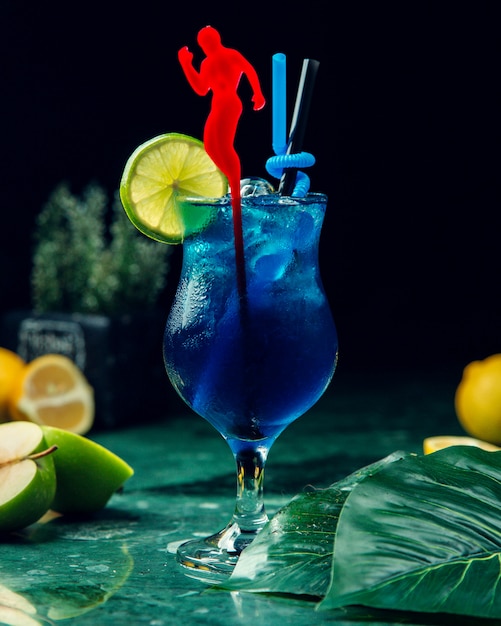 A glass of blue drink with ice garnished with lime slice