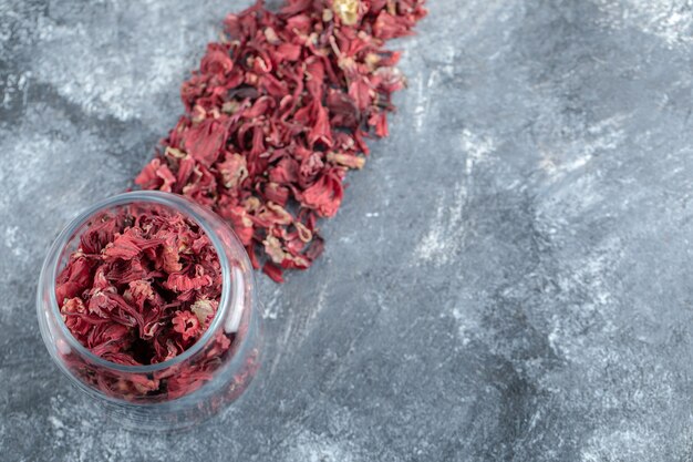 Glass bottle of dried flower petals on marble table.