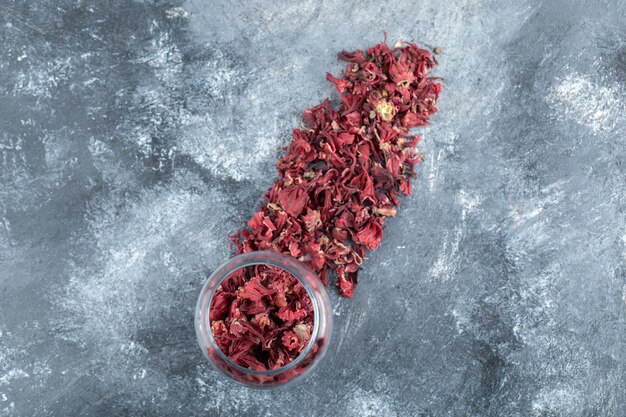 Glass bottle of dried flower petals on marble table. 