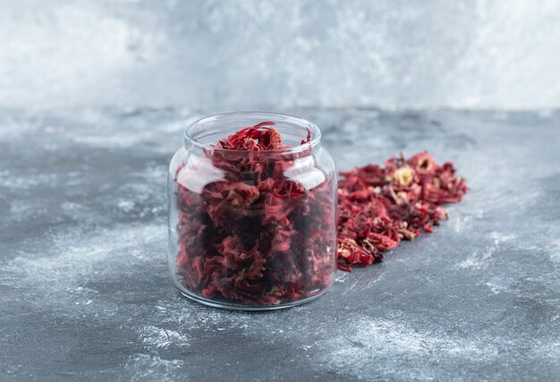 Glass bottle of dried flower petals on marble table. 
