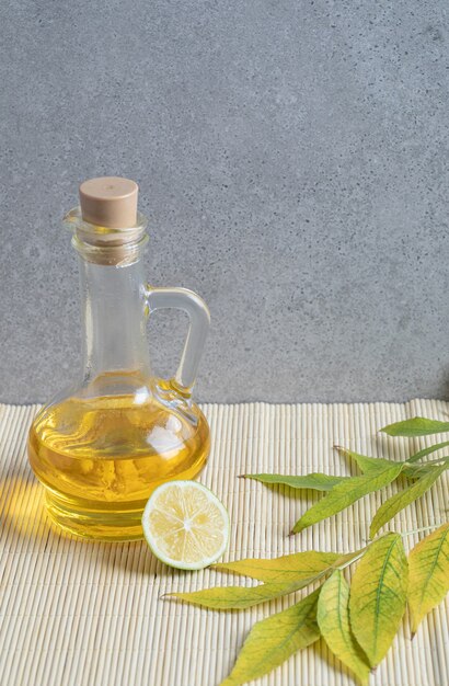 A glass bottle of oil with slice of lemon on gray background