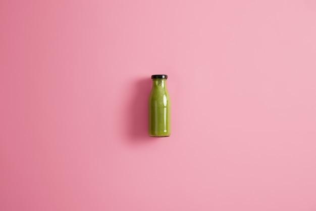 Glass bottle of refreshing smoothie made of spinach, cucumber and avocado, low in calories, isolated on pink background. Dieting and healthy lifestyle concept. Blended green vegetables for drink