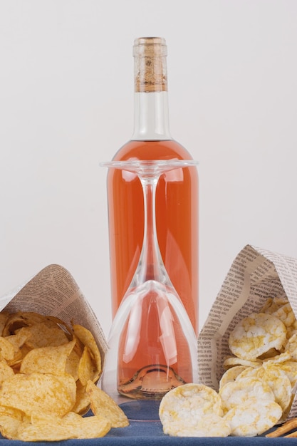 Glass and bottle of rose wine with various snack on white table.