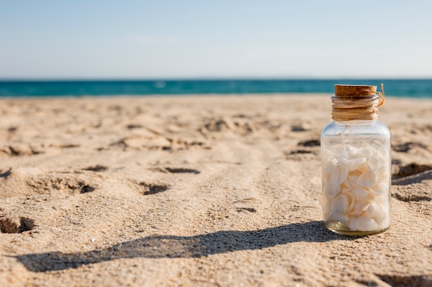 Glass bottle with seashells on sand