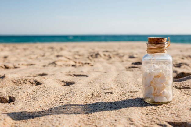 Glass bottle with seashells on sand