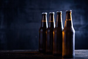 Free photo glass bottles of beer with glass and ice on dark background