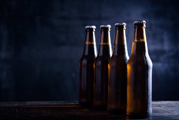 Glass bottles of beer with glass and ice on dark background