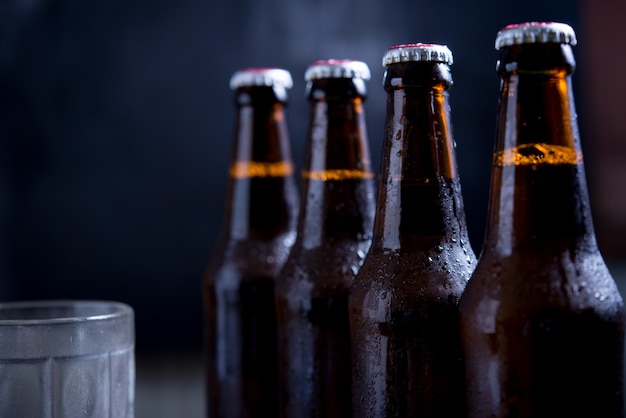 Glass bottles of beer with glass and ice on dark background