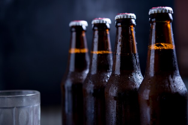 Стеклянные бутылки пива со стеклом и льдом на темном фоне