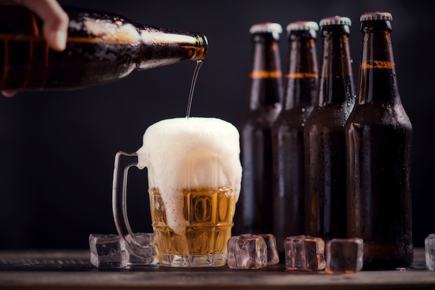 Glass bottles of beer with glass and ice on dark background