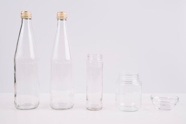 Glass bottles and cups on white background