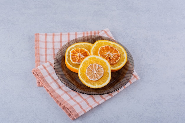 Glass bowl of fresh and dry orange slices on stone.