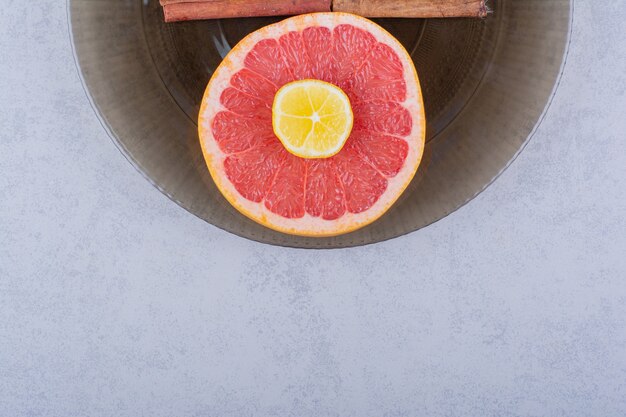 Glass bowl of fresh grapefruit slice with lemon on stone table. 