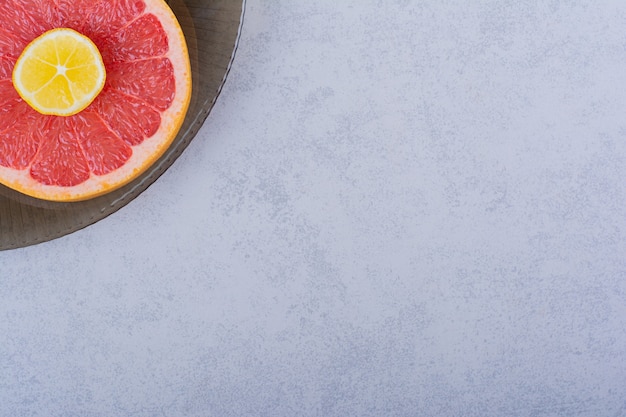 Стеклянная миска ломтика свежего грейпфрута с лимоном на камне.