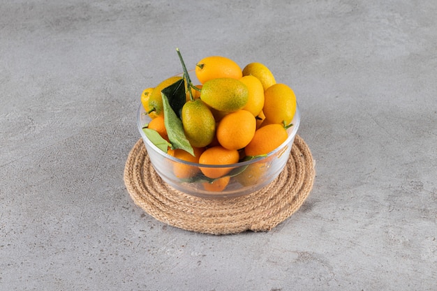 Free photo glass bowl of fresh juicy kumquats on stone surface