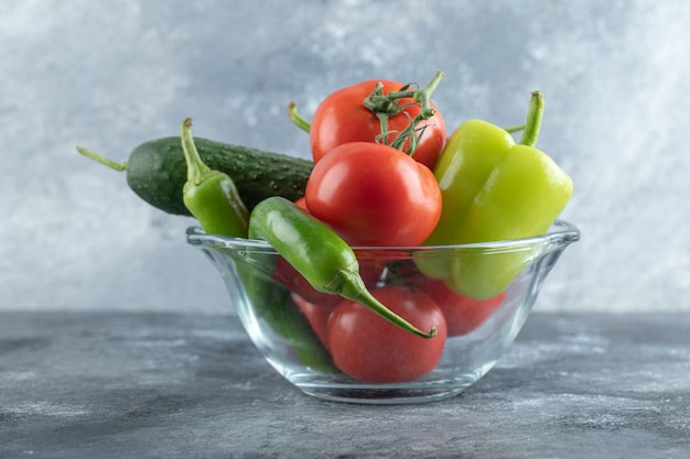 Glass bowl of fresh ripe vegetables on marble background