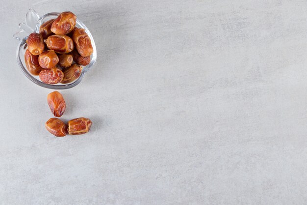 A glass bowl full of pitted dates placed on a stone table. 