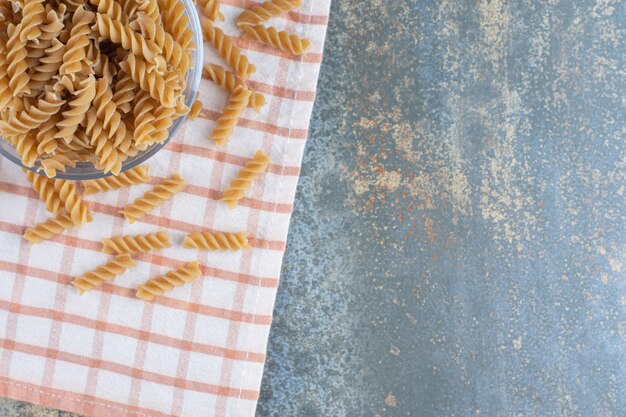 A glass bowl of fusilli pasta, on the marble surface. 