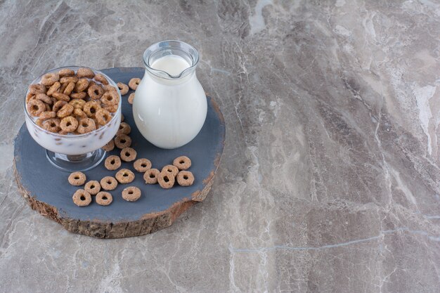 A glass bowl of healthy yogurt with crispy cereals and a glass jug of milk.