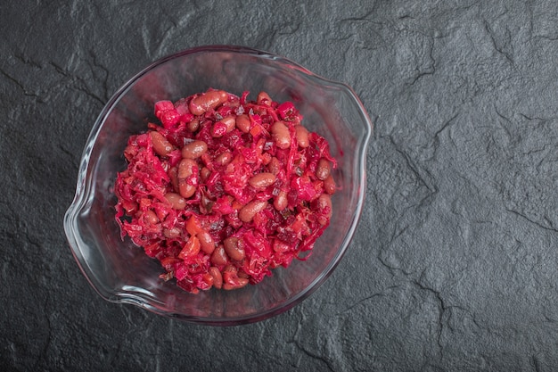 Glass bowl of pickled cabbage with red beans on black background