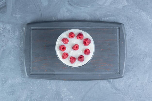 glass bowl of raspberry-topped milky rice on a navy platter on marble background. 