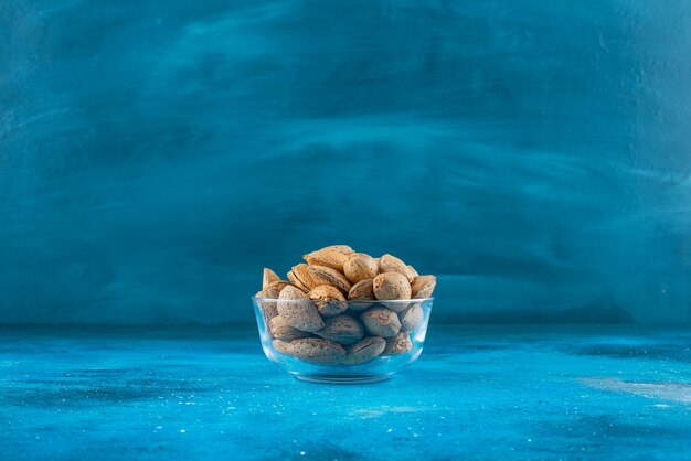 A glass bowl of shelled almonds on the blue surface