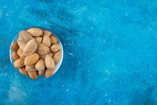 A glass bowl of shelled almonds on the blue surface