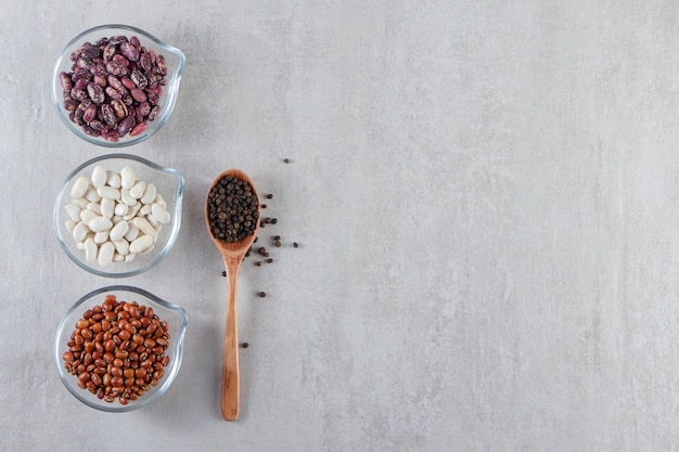 Free photo glass bowls full of various raw beans on stone background.