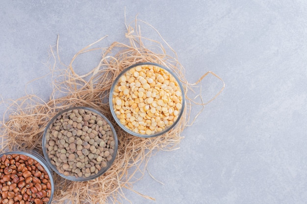 Glass bowls on a pile of straw, filled with lentils and red kidney beans on marble surface