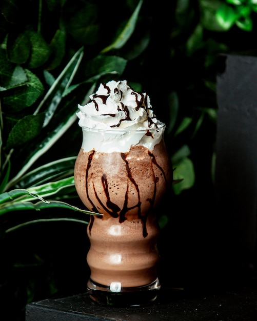 A glass of cacao drink with chocolate syrup and whipped cream