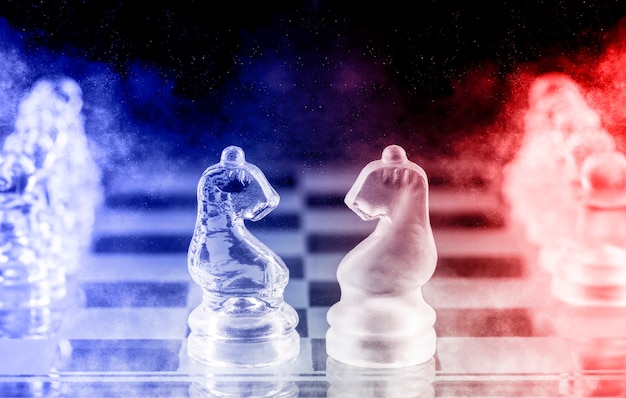 Glass chess pieces with blue and red light on a glass chessboard with reflection, on a black background.