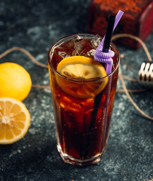 a glass of coca-cola with ice cubes and lemon slice in grey background