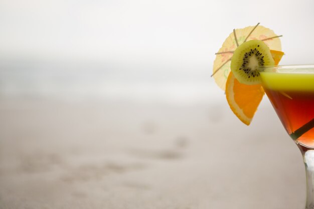 Glass of cocktail drink garnished with kiwi, lime and cocktail umbrella