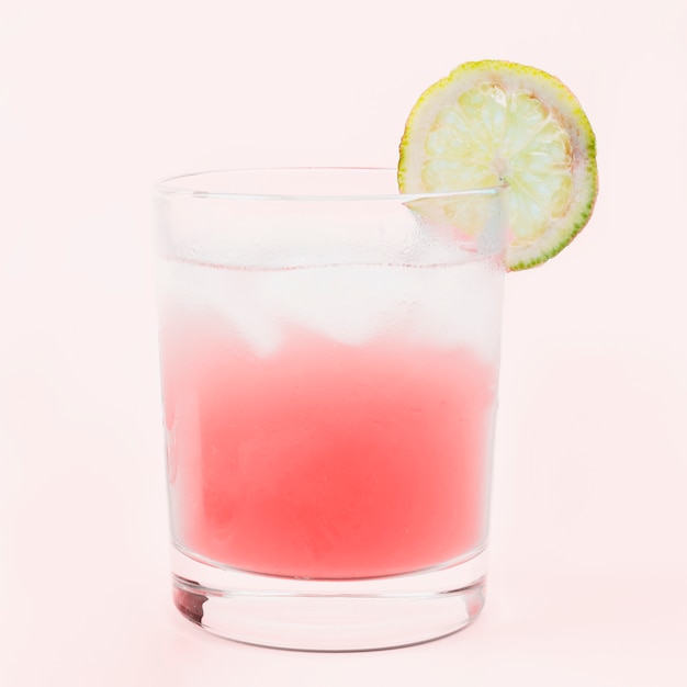 Стакан коктейля с ломтиком лимона на розовом фоне