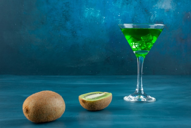 Foto gratuita bicchiere di cocktail e kiwi freschi sulla superficie blu.